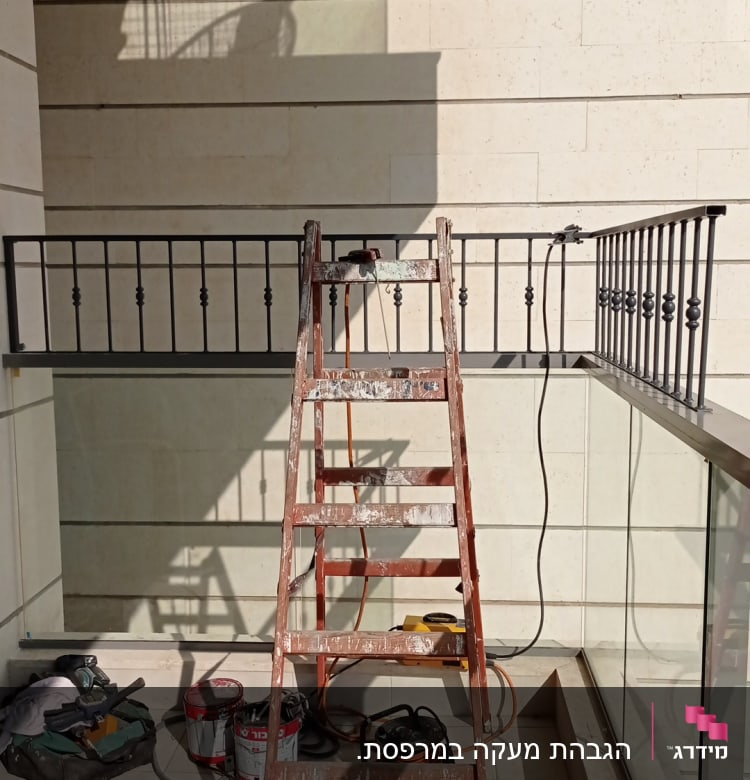 סולם עץ מול מעקה מתכת עם כלים על הרצפה